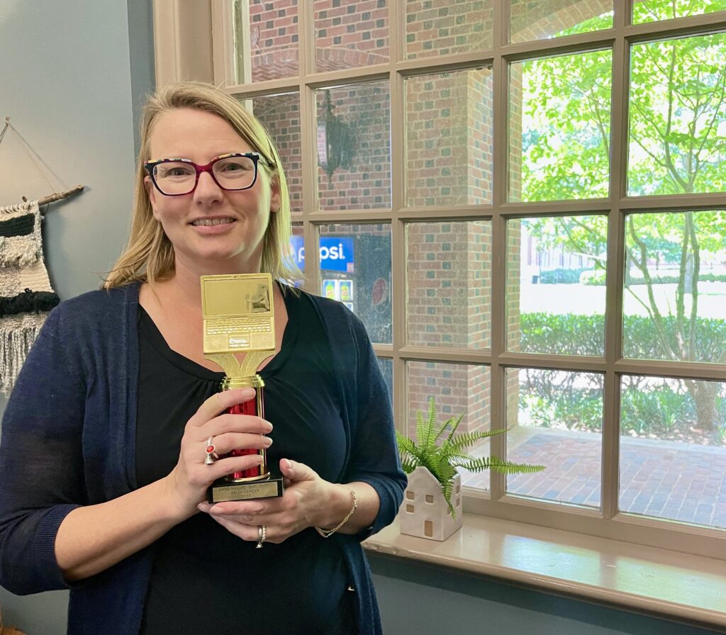 Kelly Denzer holding red and gold award.