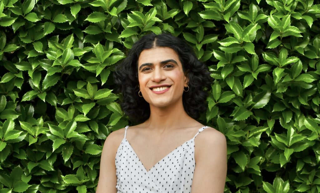 Image of Zara Rao smiling in front of a green shrub. 