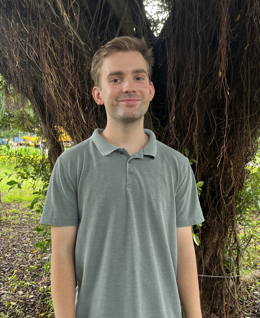 Photo of Andrew Denny wearing a green polo in front of a brown tree